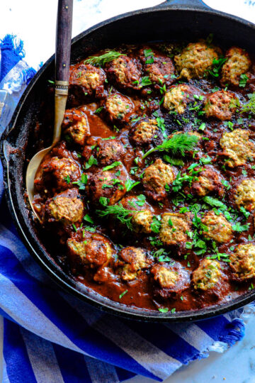 spicy ground chicken meatballs with baharat in cast iron skillet with serving spoon and blue napkin
