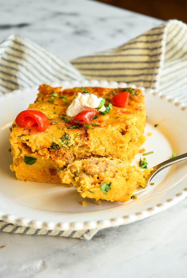 cornbread breakfast casserole on white plate with a bite on fork and blue striped napkin in background