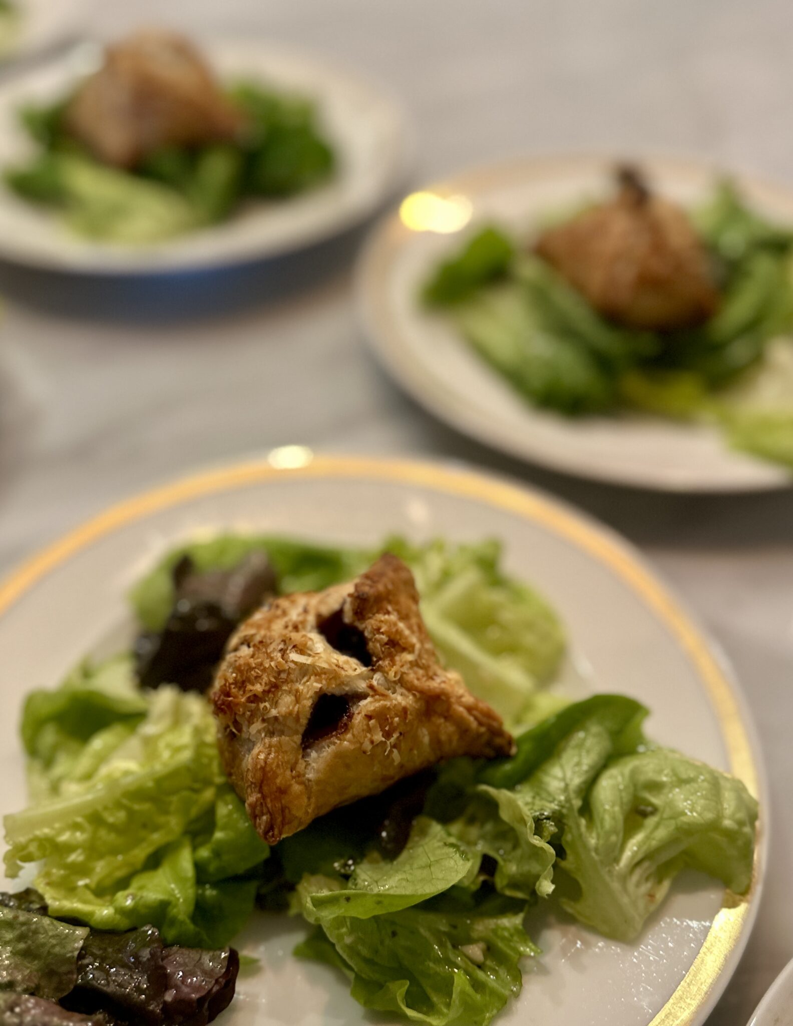Boston Lettuce Salad with Brie filled Puff Pastry and caramelized onions on white plates with gold rim