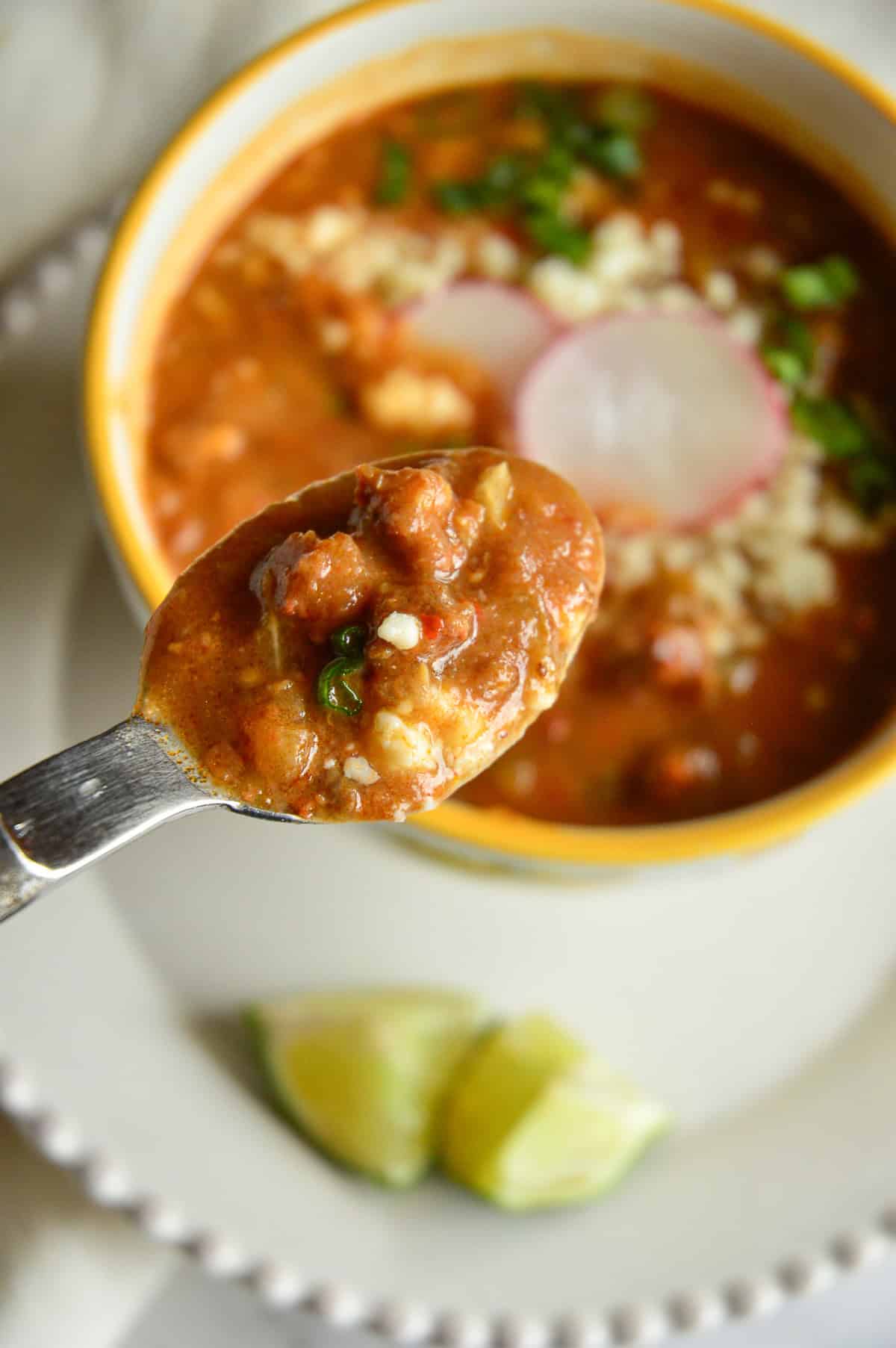 spoon of refried bean soup being held over yellow rimmed bowl