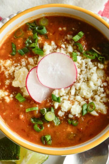 Refried bean soup sprinkled with cotija cheese and scallions in a yellow rimmed bowl with sliced radishes