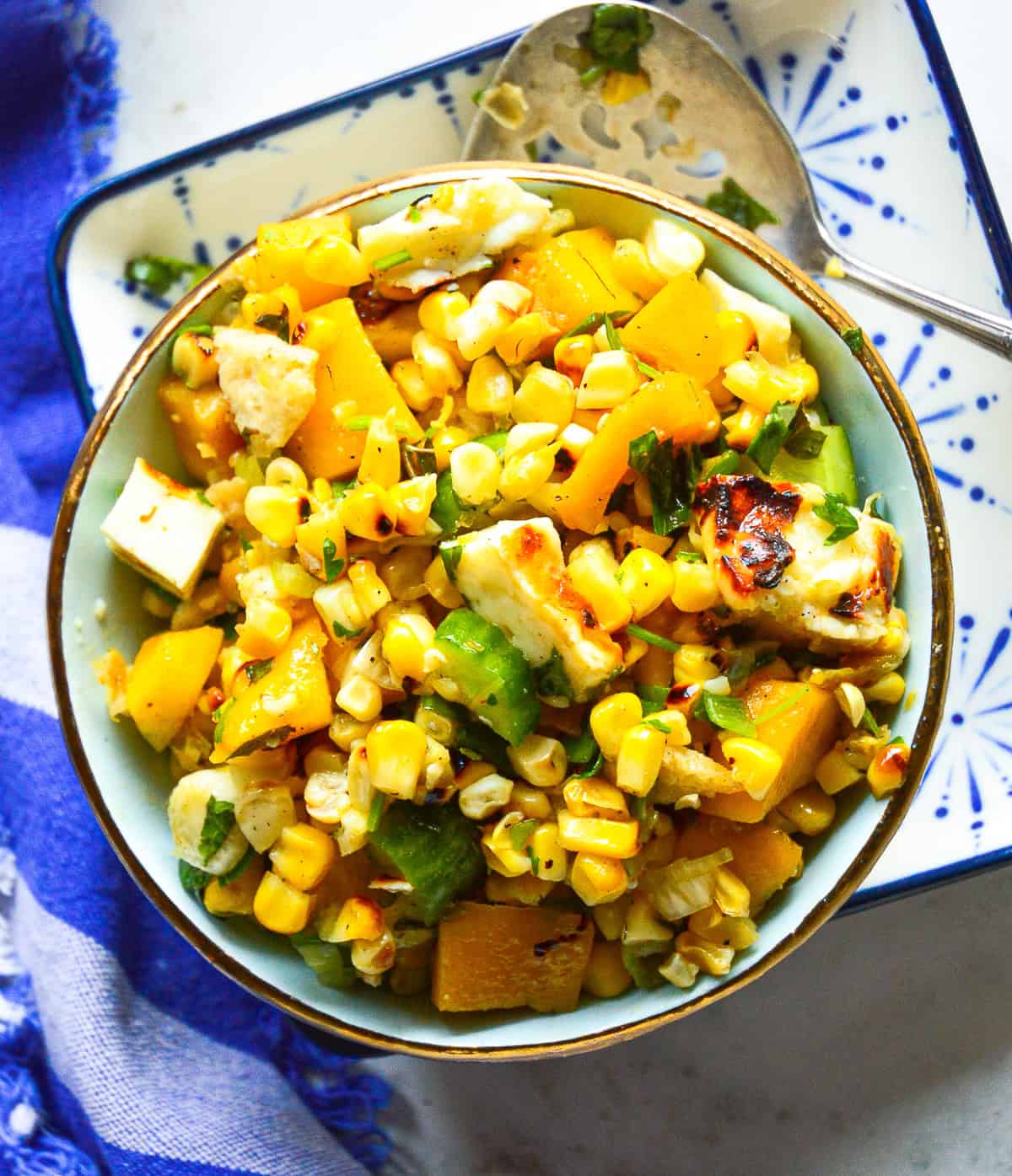 roasted corn salad with halloumi cheese, mango and cucumbers in blue bowl