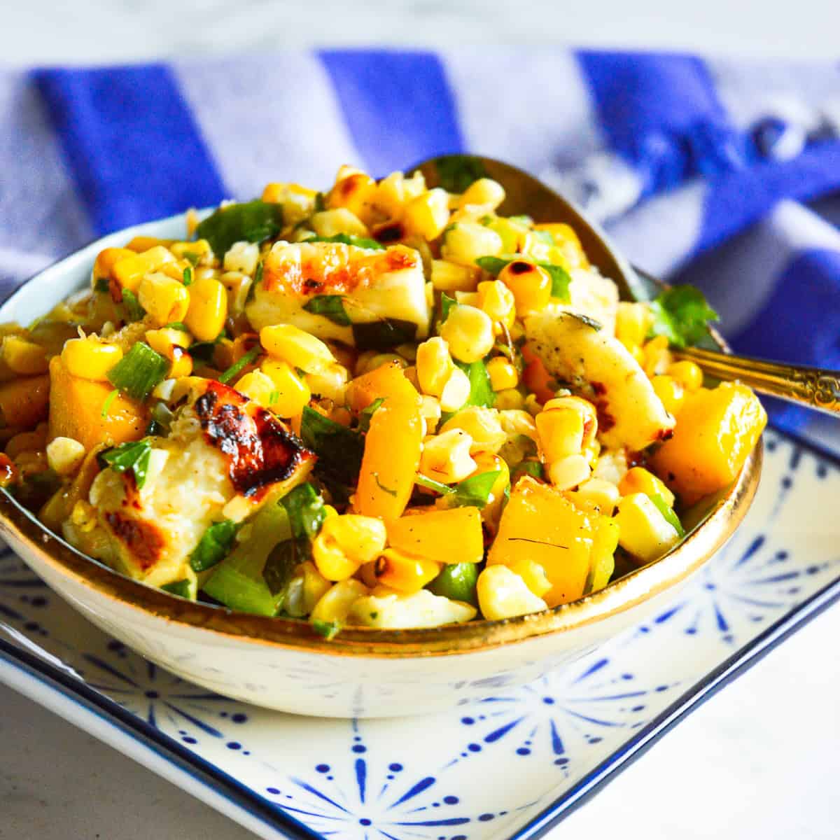 roasted corn salad with mango and halloumi on square blue plate with blue striped napkin in background