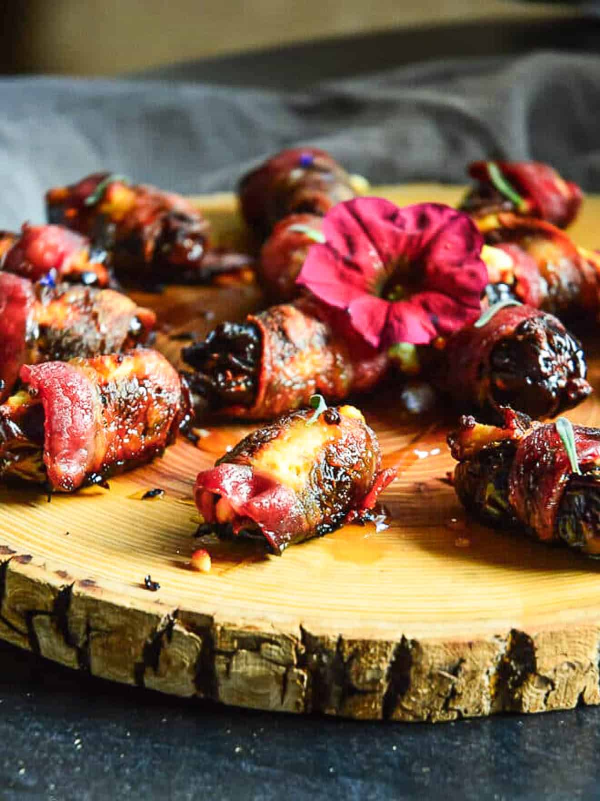 bacoon wrapped dates stuffed with goat cheese on a log round with petunia garnish