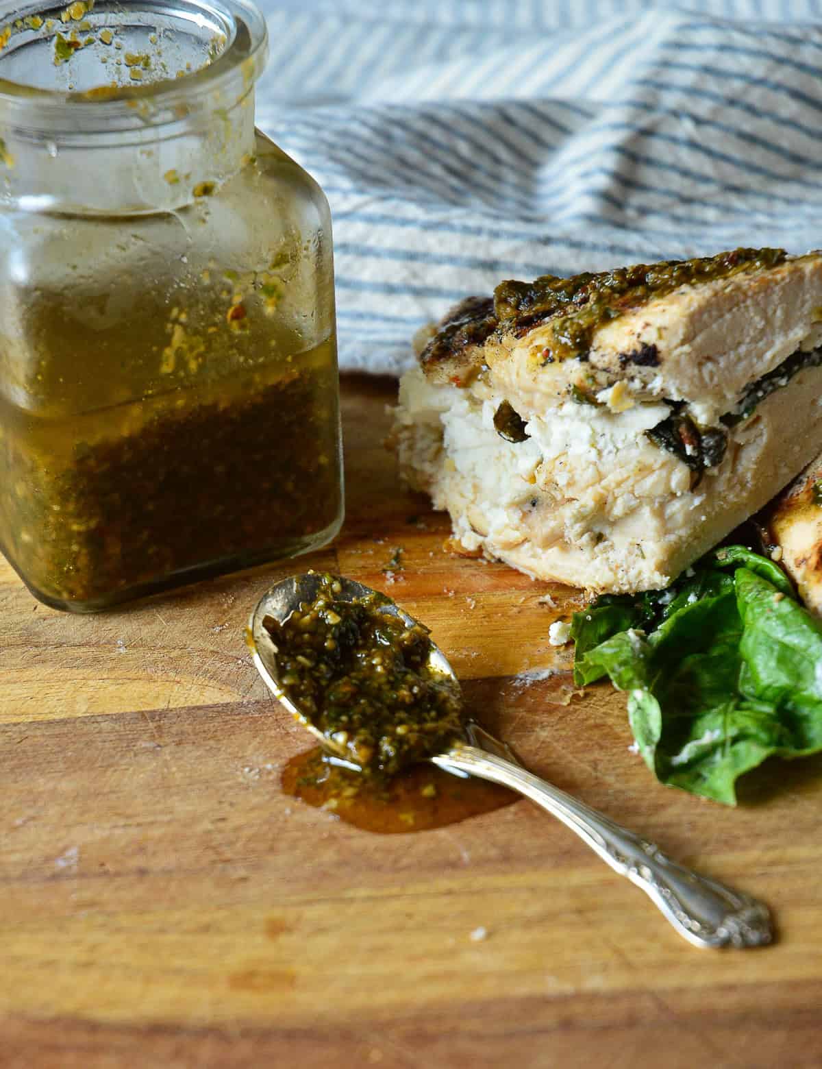 chicken with goat cheese and jar of basil vinaigrette with spoon of dressing on wood cutting board