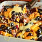 baked french toast casseerole with blueberries and condensed milk in white ceramic dish