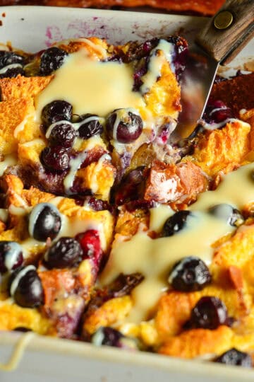 baked french toast casseerole with blueberries and condensed milk in white ceramic dish
