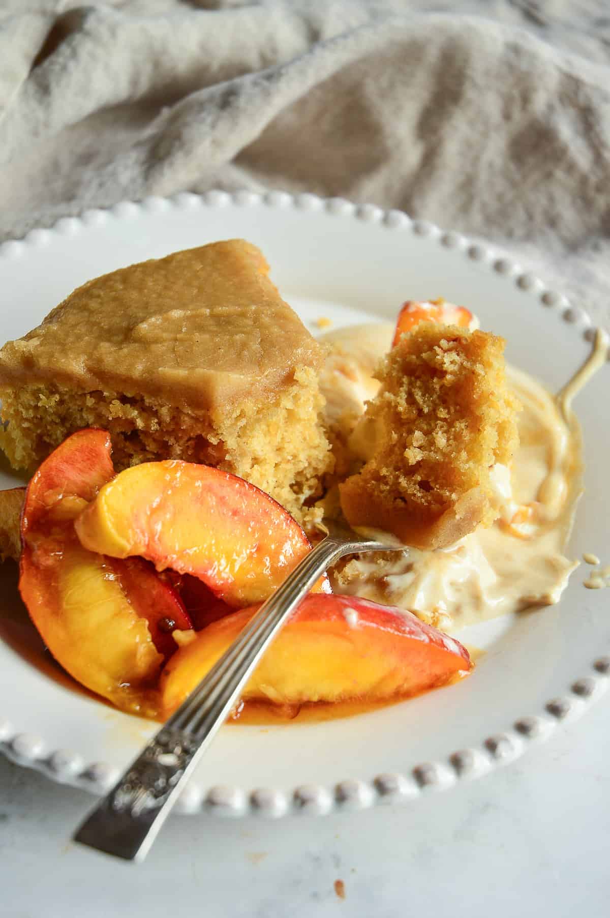 buttermilk cake recipe with brown butter brown sugar frosting on white plate with  a fresh peach toppping with a sour cream brown sugar sauce 