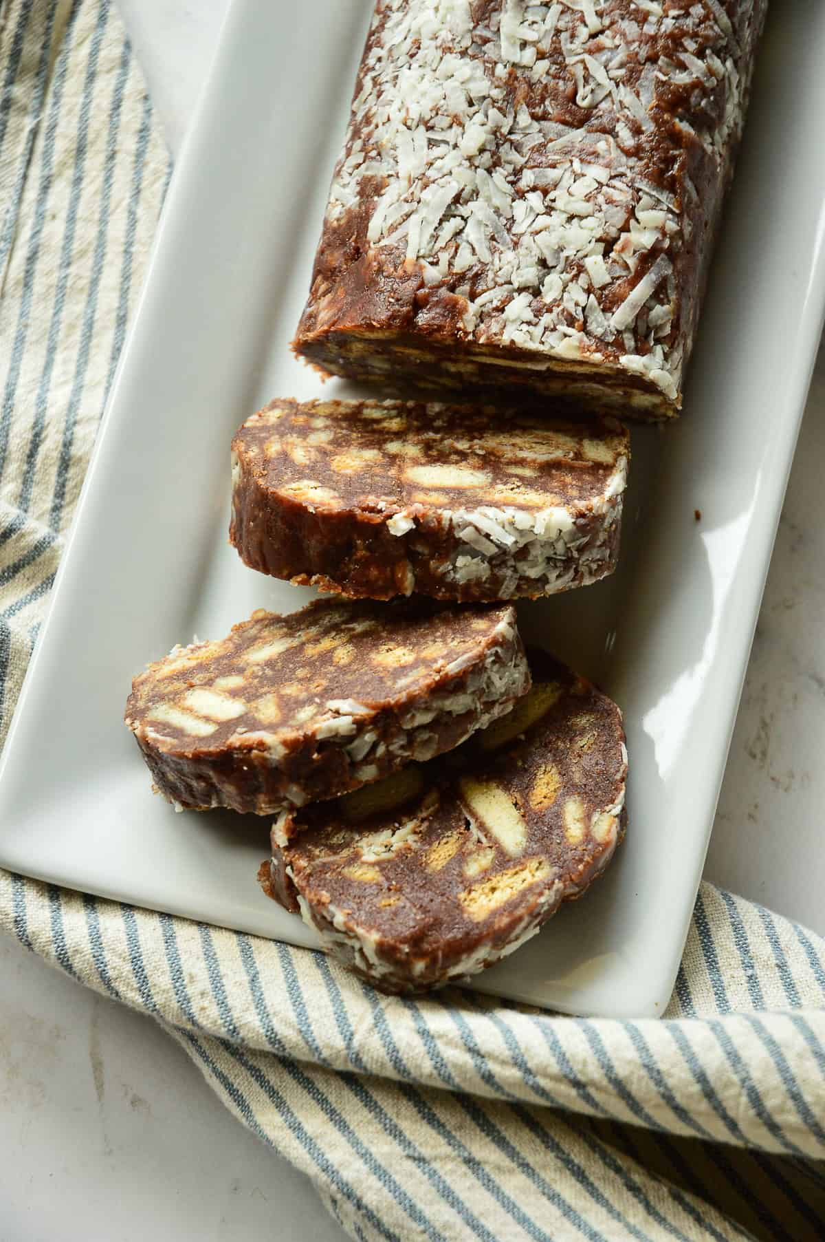 chocolate salami slices and cylindrical log on white plate with blue stripe napkin