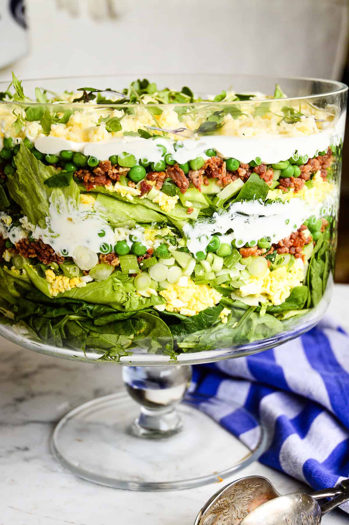 layered salad in green in tall glass bowl with blue striped napkin