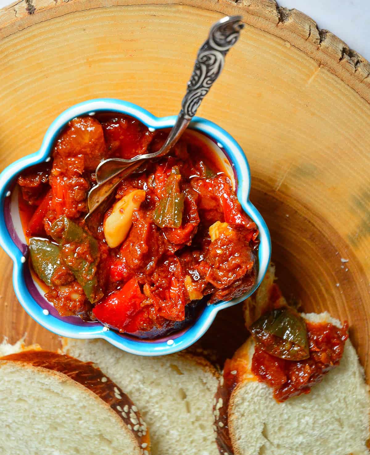 tomato matbucha on wood round with sliver spoon and challah