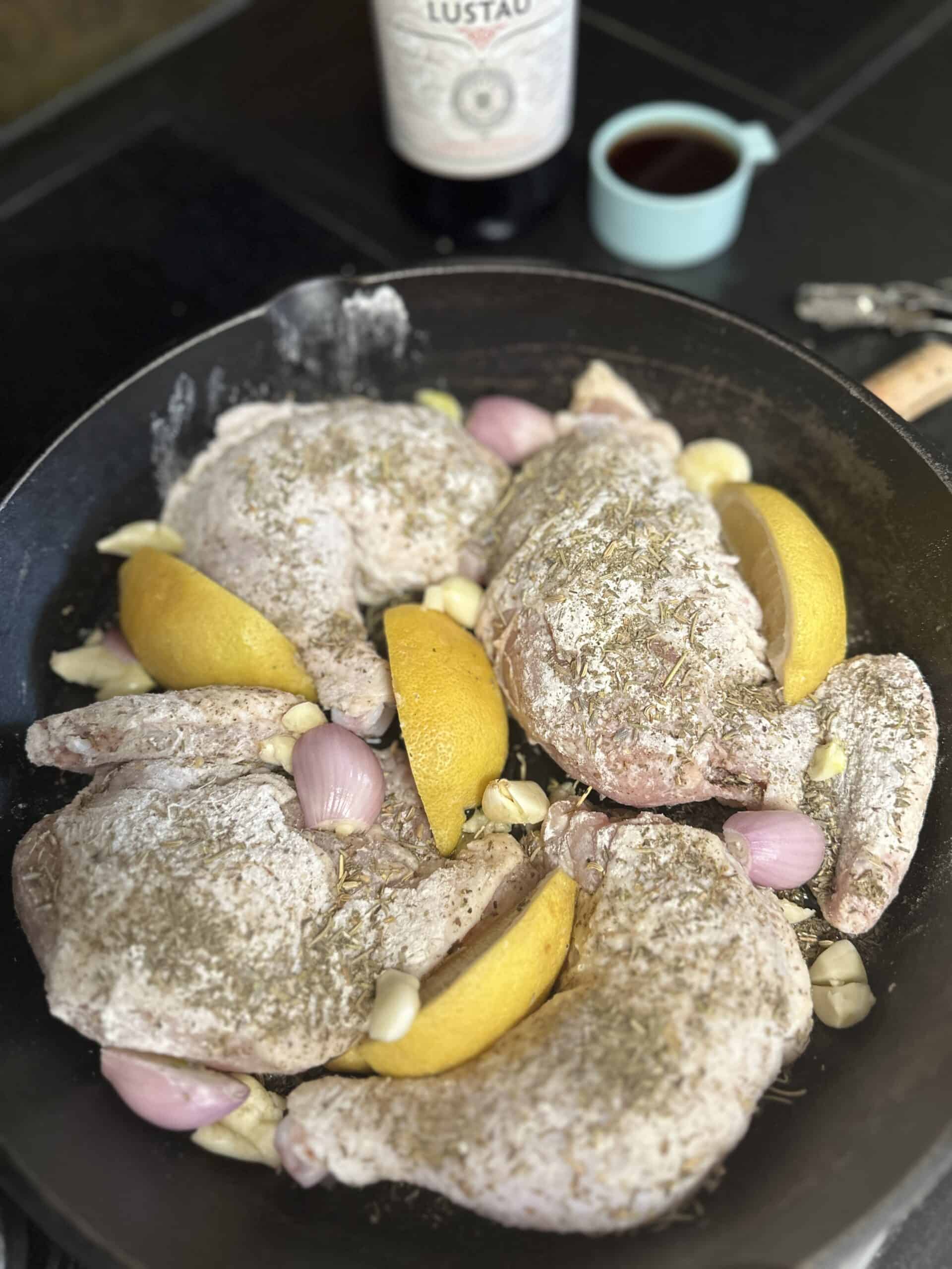 chicken provencal in cast iron skillet before being baked with red vermouth in background