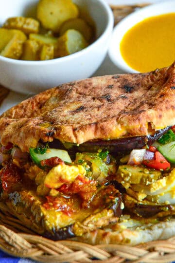 sabich eggplant and hard boiled egg pita on straw plate with pickles and amba