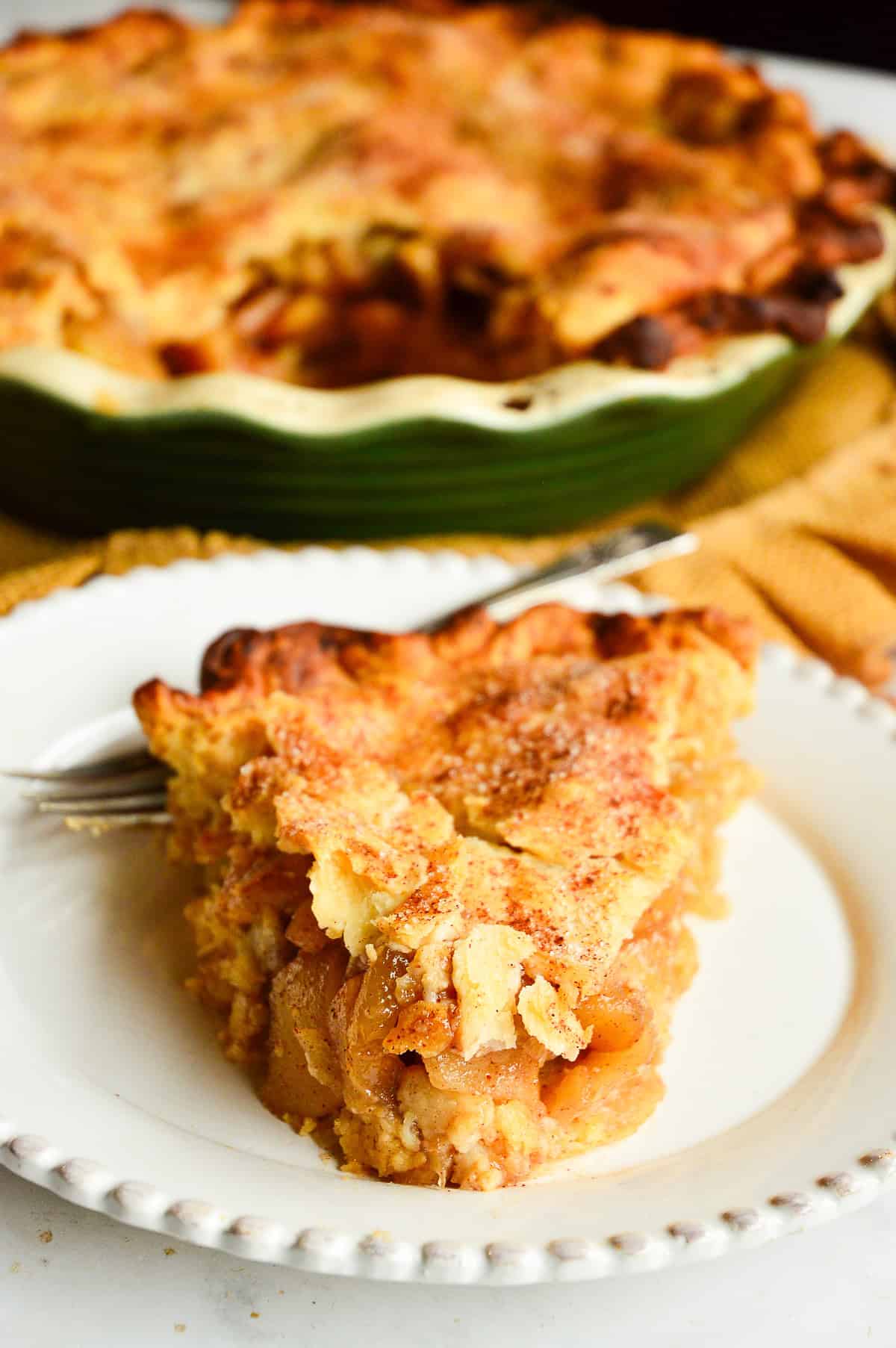 Slice of Pillsbury Apple pie recipe on white plate with fork and green pie plate in background