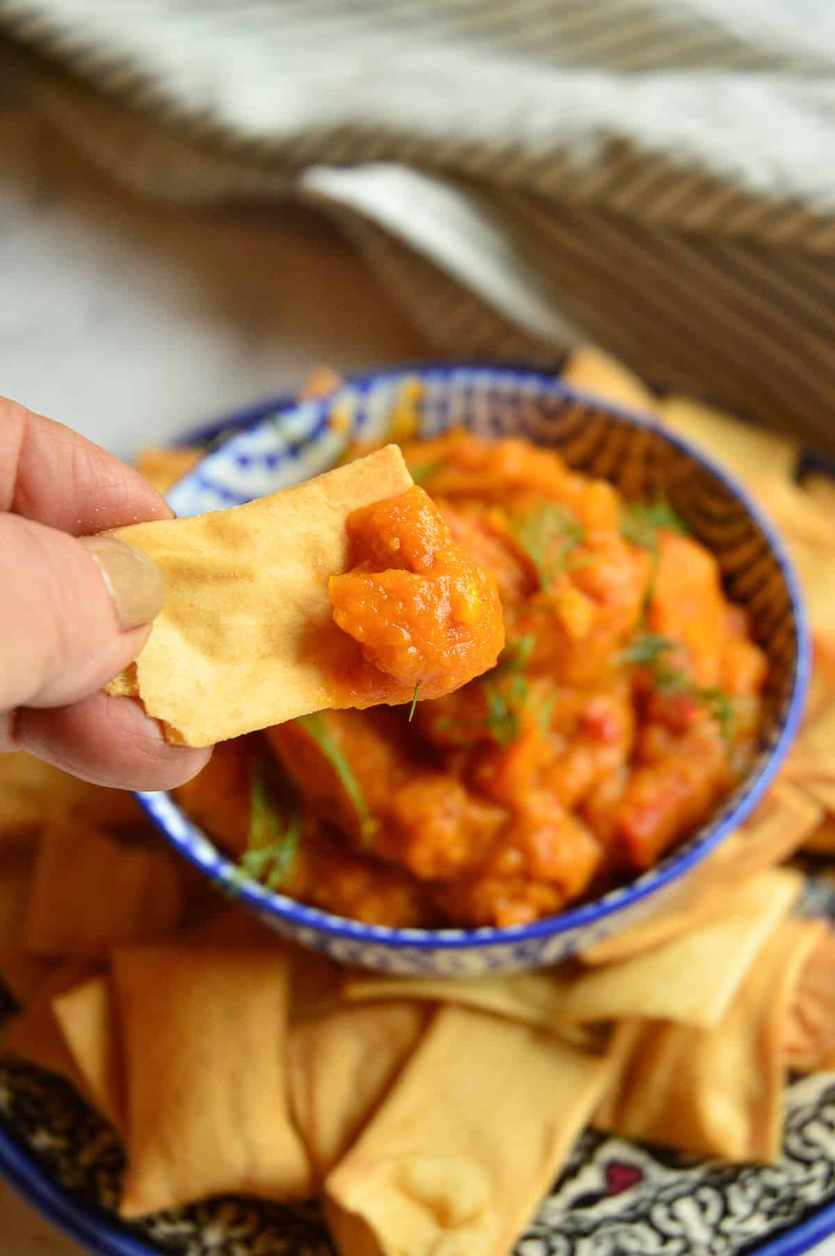 garlic pumpkin dip tershi on pita chip held over bowl of dip