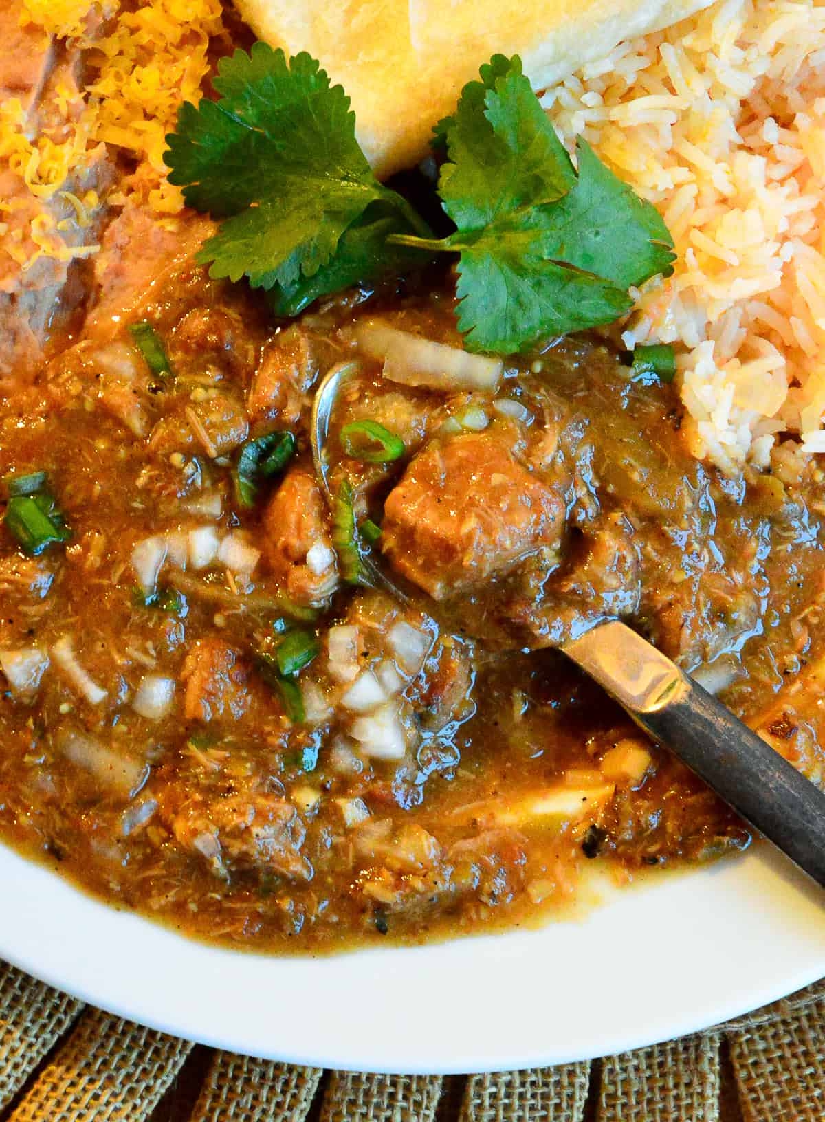 green chili with pork on plate with spoon and rice and beans