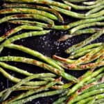 oven roasted green beans on black baking sheet with salt
