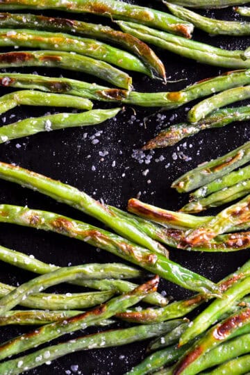 oven roasted green beans on black baking sheet with salt