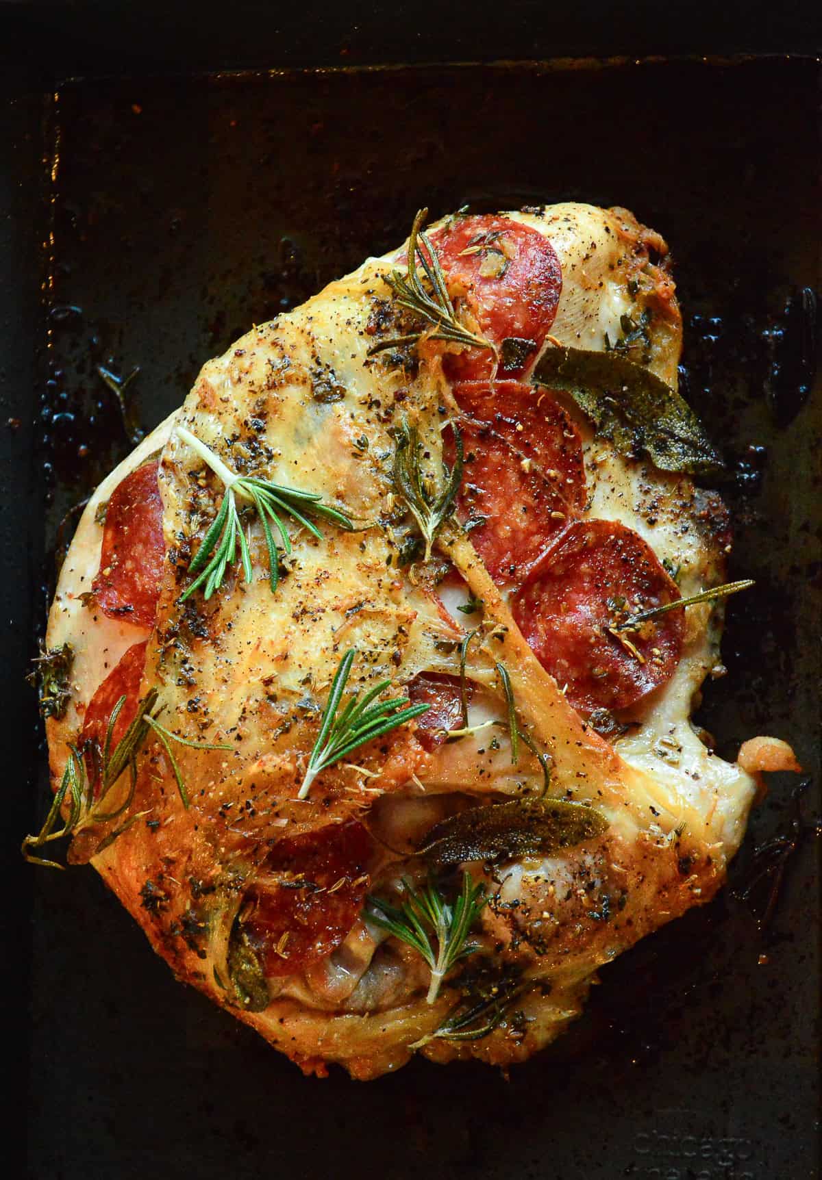 buttery bone-in turkey breast with pepperoni and herbs in black pan