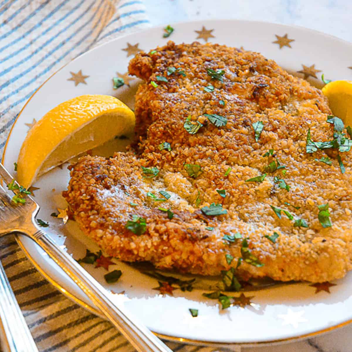 chicken schnitzel recipe on white plate with gold star and lemon wedges