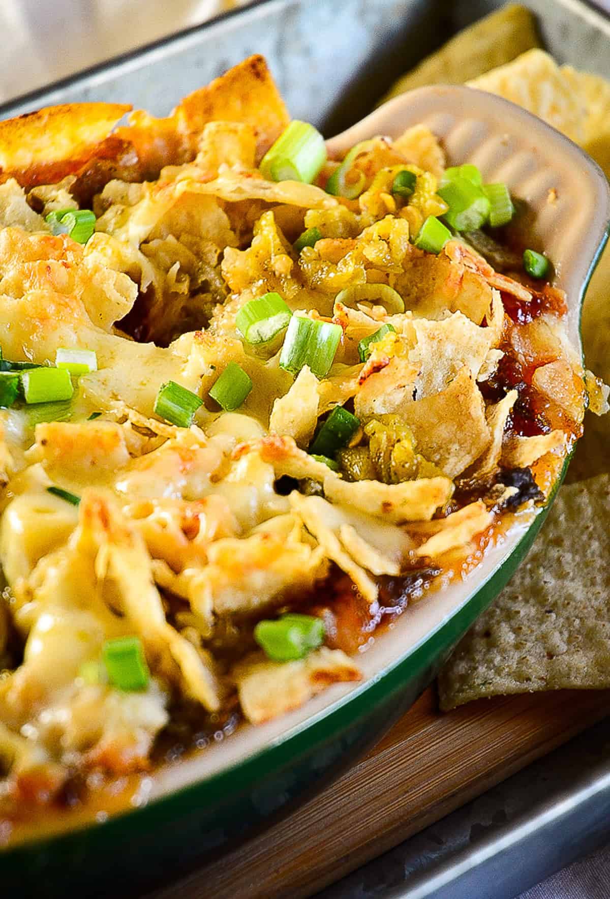 chili pepper jam dip with tortilla chips and green chilies in green oval baking dish
