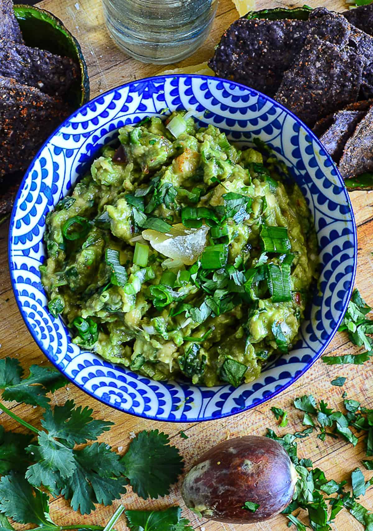 guacamole with dried pineapple and scallions and tequila in blue and white bowl with blue corn chips