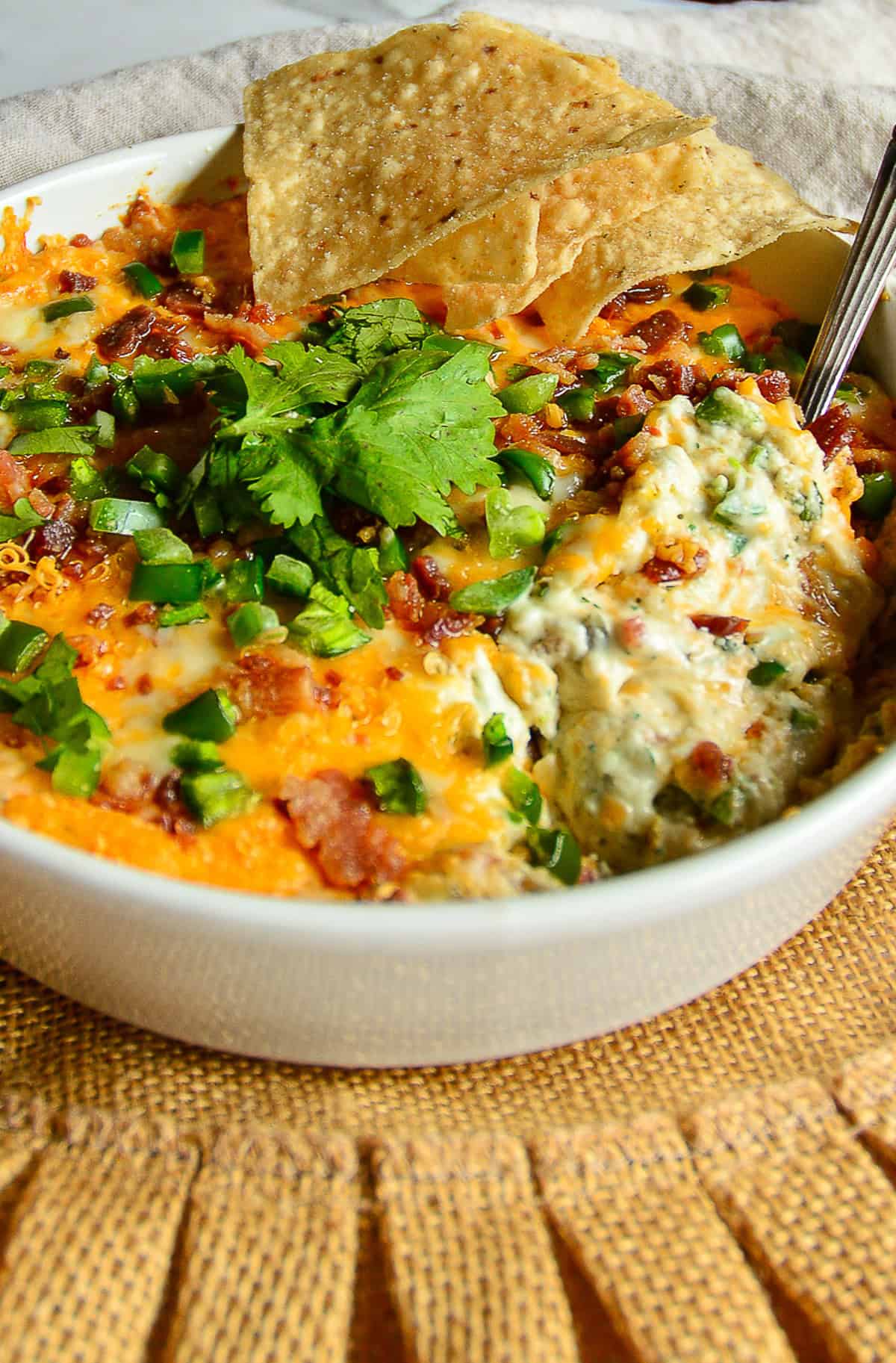 jalapeno popper dip with scallions and cilantro and bacon garnish in white casserole dish with corn chips