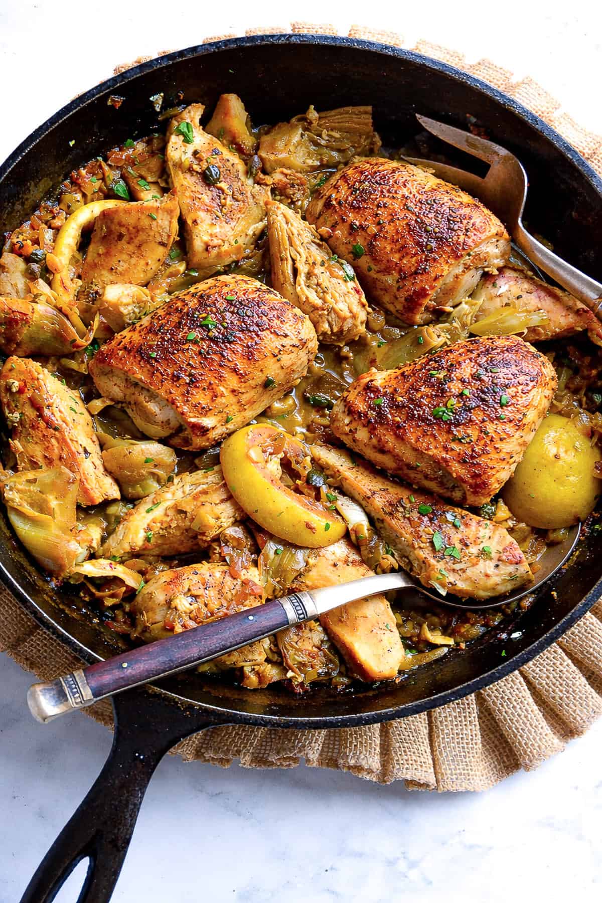chicken with artichoke hearts recipe in cast iron skillet with serving spoon and fork