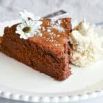 flourless chocolate date cake recipe slice on white plate with flowers and whip cream