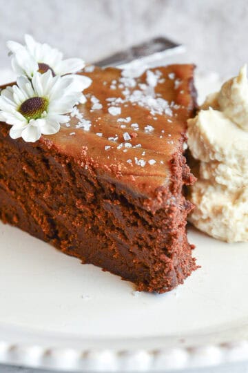 flourless chocolate date cake recipe slice on white plate with flowers and whip cream