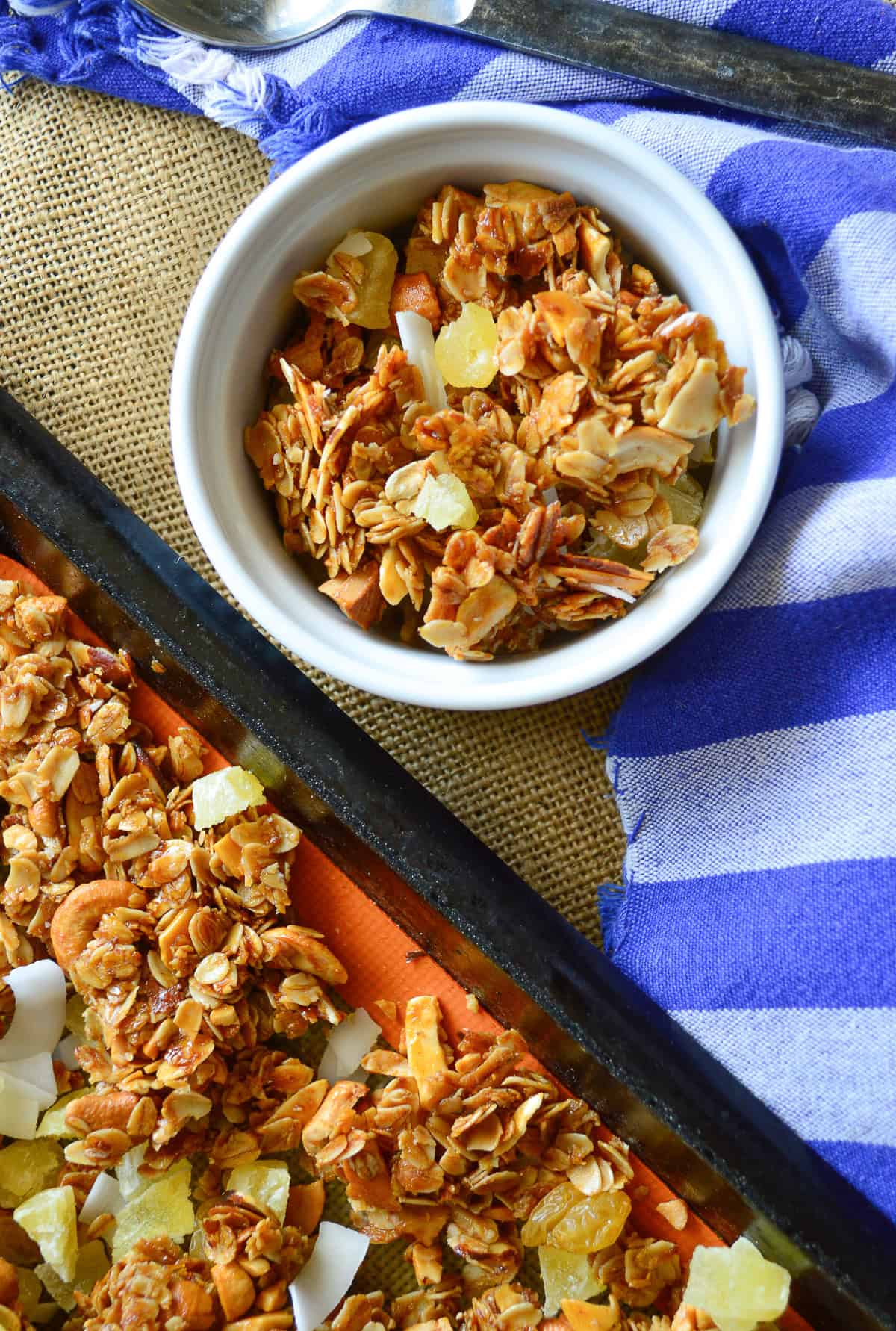 granola with coconut, pineapple and cashews in white bowl with blue napkins
