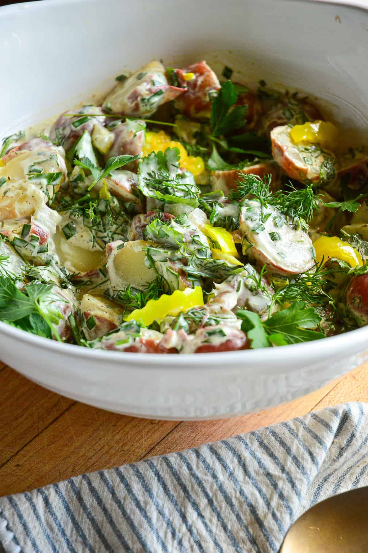 potato salad with pickles and pepperoncini with fresh dill and parsley and chives in white bowl