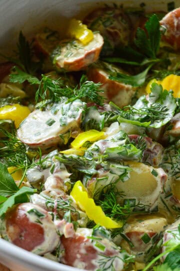 dill pickle herby potato salad with peepperoncini in white bowl