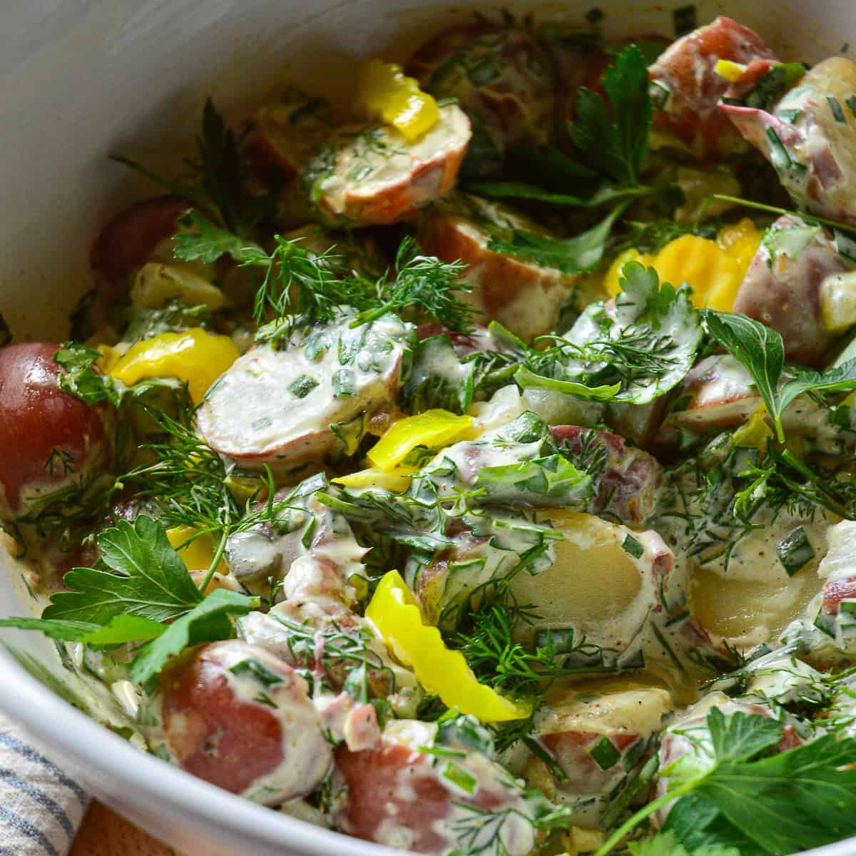 dill pickle potato salad with fresh herbs and pepperoncini in white bowl
