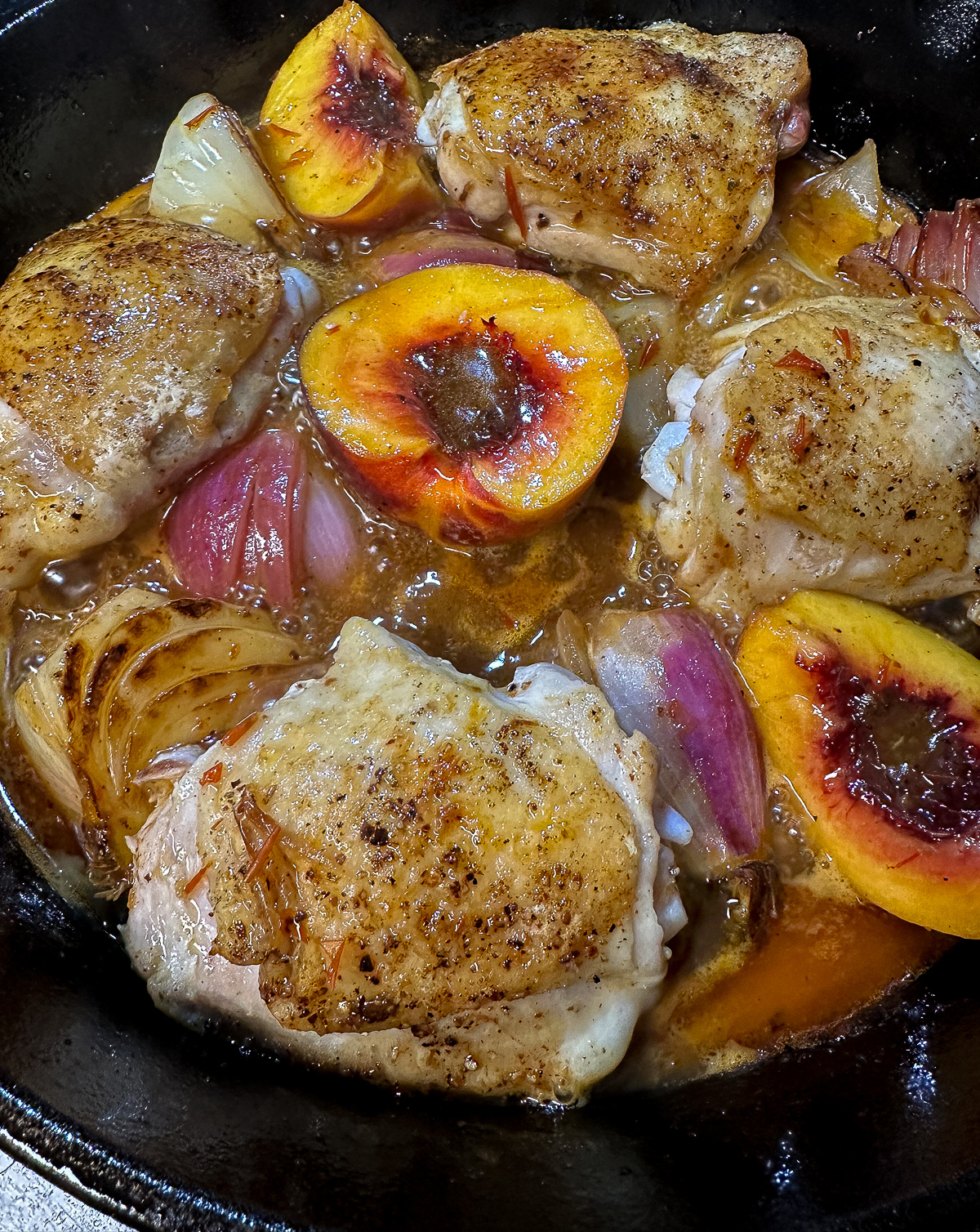 chicken cooking in harissa honey sauce in cast iron pan with onions and peaches