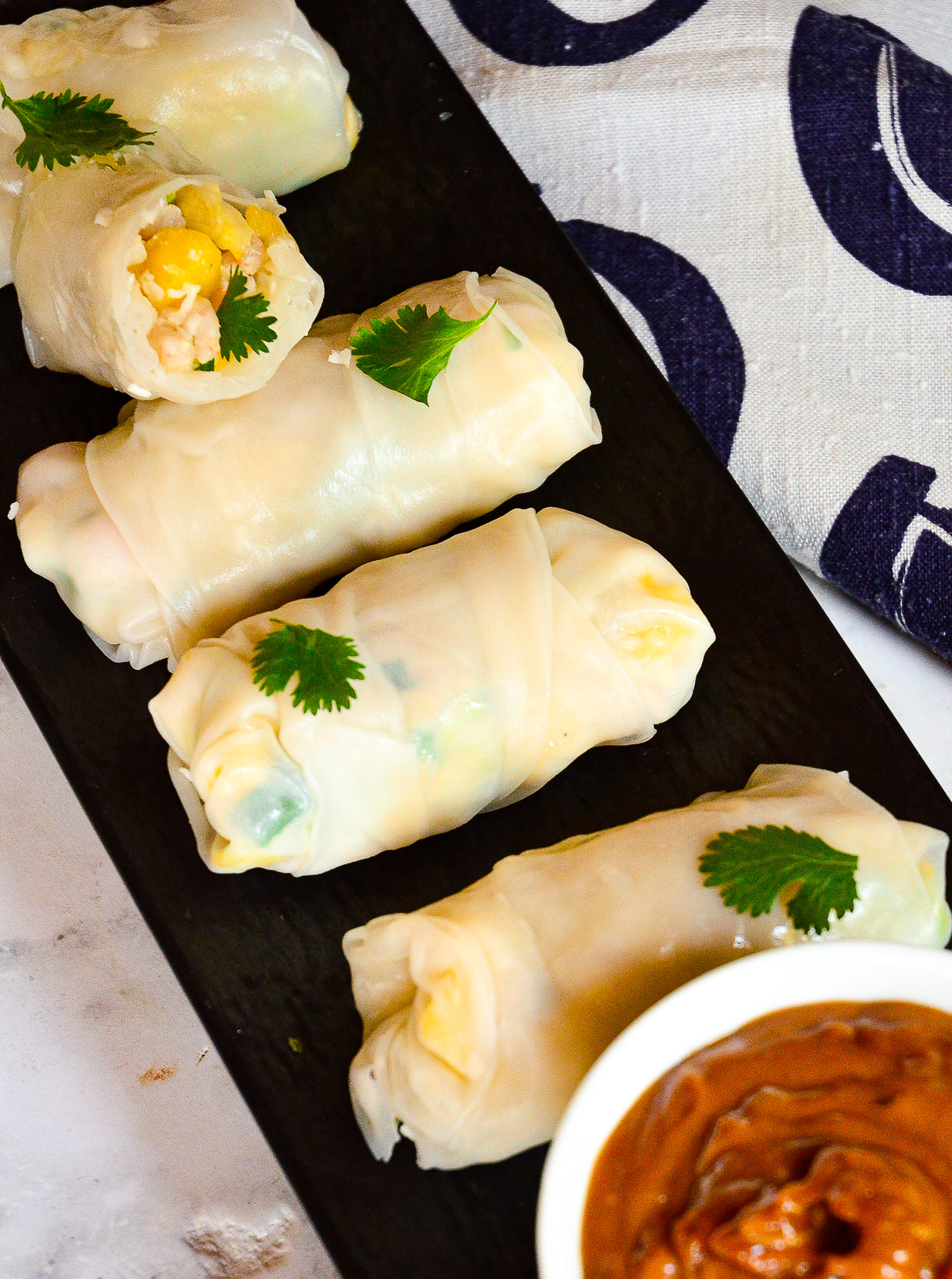 Vietnamese rice paper rolls with shrimp, mango and coconut on black platter with peanut sauce