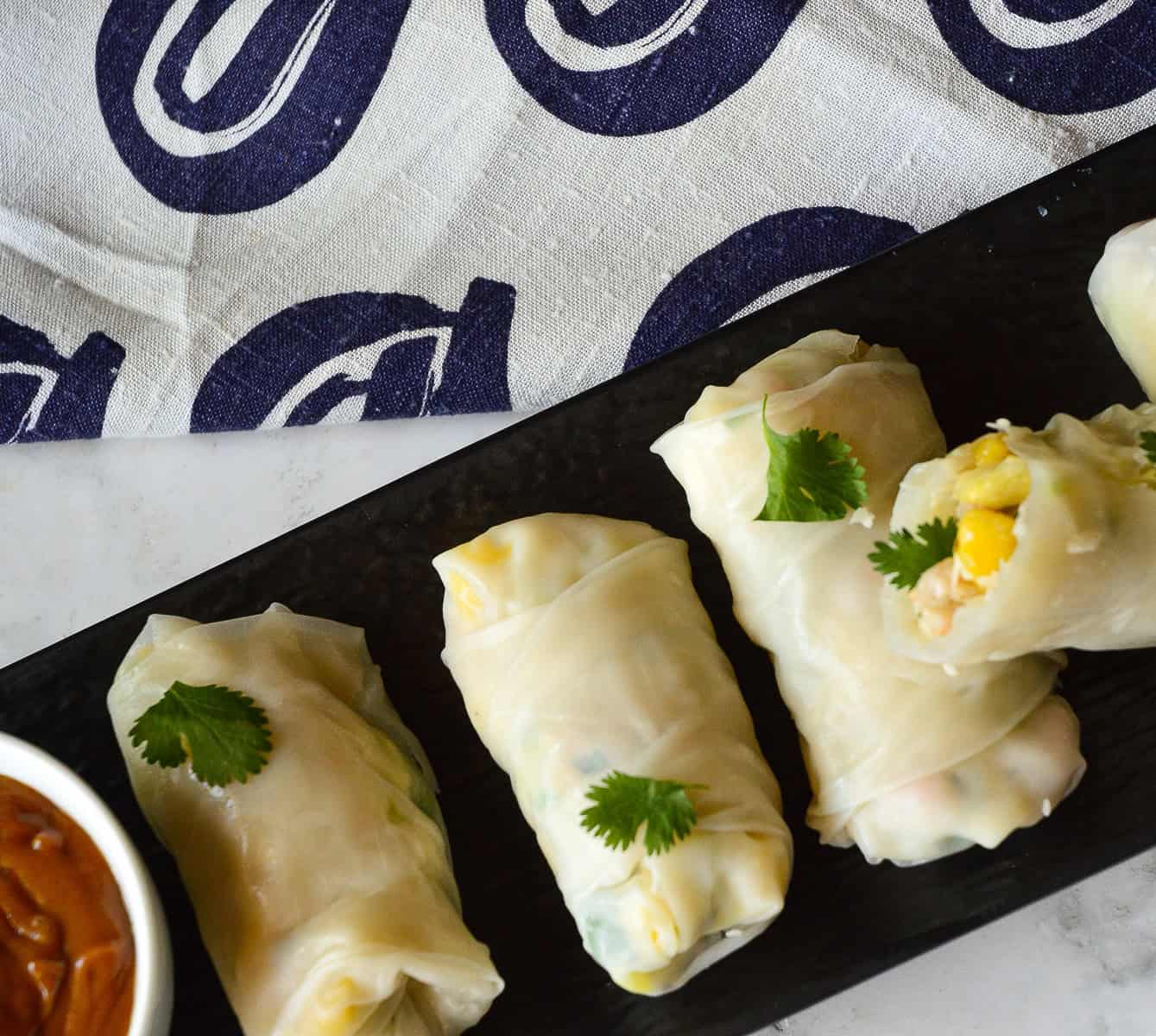 Vietnamese rice paper rolls with shrimp, mango and coconut on black platter with peanut sauce